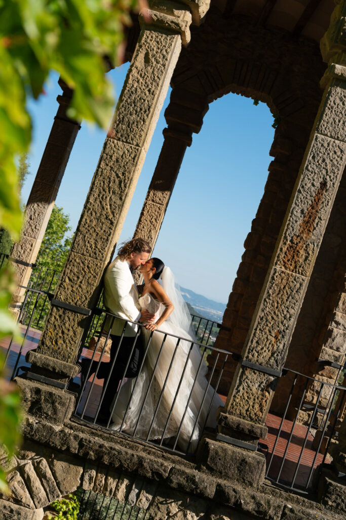 Newlyweds kissing under stone archway. | Gabys Films